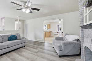 Living area featuring a fireplace, light wood-style floors, and ceiling fan