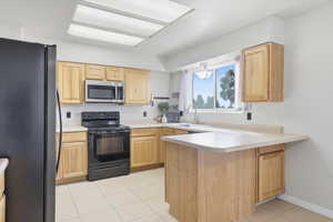 Kitchen featuring a peninsula, black appliances, light tile patterned flooring, light countertops, and light brown cabinetry