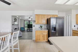 Kitchen featuring stainless steel fridge, light countertops, light tile patterned floors, a brick fireplace, and light brown cabinetry
