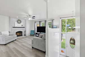 Living room featuring light wood finished floors, a fireplace, and ceiling fan