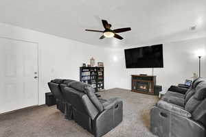 Carpeted living room with ceiling fan and a lit fireplace