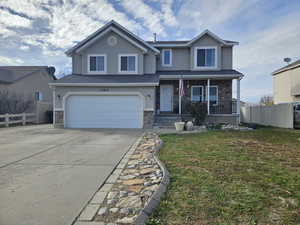 Traditional-style home featuring stone siding, a porch, an attached garage, concrete driveway, and stucco siding