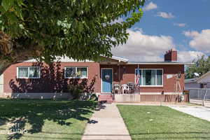 View of front facade with a front yard, a chimney, and brick siding