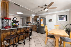 Kitchen featuring ornamental molding, stainless steel fridge with ice dispenser, a breakfast bar, light tile patterned floors, and ceiling fan