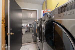 Laundry room featuring light tile patterned flooring, washing machine and dryer, and a textured ceiling