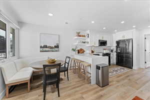 Kitchen featuring open shelves, white cabinets, black appliances, a peninsula, and light wood-style flooring