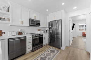 Kitchen with open shelves, stainless steel appliances, white cabinets, recessed lighting, and light wood-style flooring
