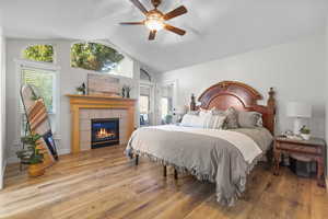 Primary Bedroom featuring lofted ceiling, wood finished floors, a fireplace, and ceiling fan