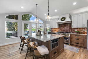Kitchen with decorative backsplash, granite counters, vaulted ceiling, french doors, and an island with  sink