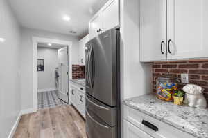 Kitchen with freestanding refrigerator, decorative backsplash, light wood finished floors, white and natural wood cabinets, and granite countertops