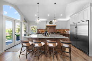 Kitchen featuring lofted ceiling, stainless steel built in refrigerator, recessed lighting, backsplash, and light stone counters