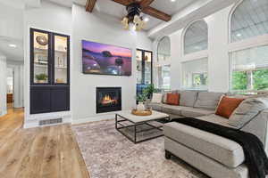 Living area featuring light wood-type flooring, beam ceiling, a glass covered fireplace, recessed lighting, and a ceiling fan