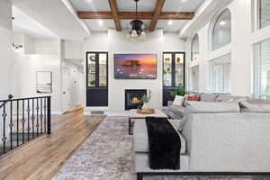 Living area featuring beamed ceiling, light wood-style flooring, a high ceiling, a glass covered fireplace, and coffered ceiling