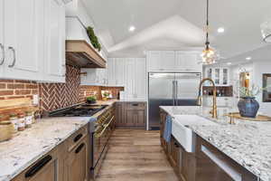 Kitchen featuring lofted ceiling, decorative light fixtures, high quality appliances, light stone counters, and white cabinets