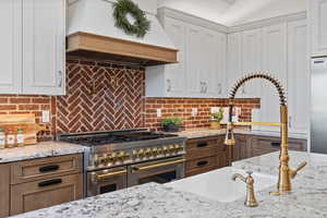 Kitchen featuring white and natural wood cabinetry, granite countertops, high quality appliances, custom range hood, and tasteful backsplash