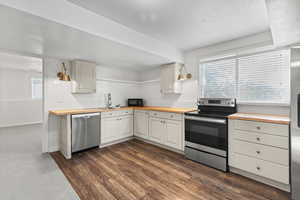 Kitchen with appliances with stainless steel finishes, wood counters, dark wood-type flooring, and open shelves