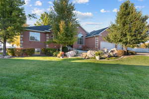View of property hidden behind natural elements featuring brick siding, a front lawn, a garage, and a patio area
