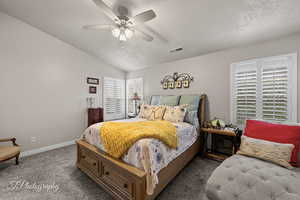 Carpeted bedroom featuring vaulted ceiling, a textured ceiling, and a ceiling fan