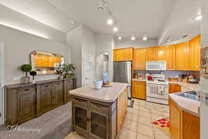 Kitchen with lofted ceiling, white appliances, a kitchen island, light tile patterned flooring, and backsplash
