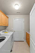 Laundry area featuring cabinet space, a textured ceiling, and washing machine and dryer