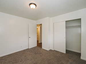 Unfurnished bedroom featuring dark carpet, a textured ceiling, and a closet