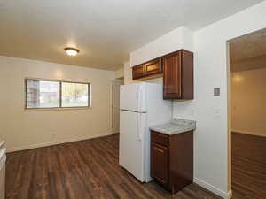 Kitchen with a textured ceiling, light countertops, freestanding refrigerator, dark wood-style floors, and dark brown cabinets
