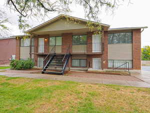 View of front of home featuring brick siding, a front lawn, and stairs