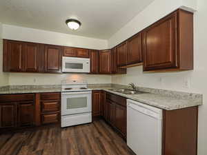 Kitchen with white appliances, a textured ceiling, light countertops, dark wood-style flooring, and dark brown cabinetry