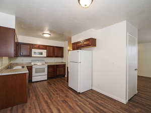 Kitchen with white appliances, light countertops, a textured ceiling, and dark wood-style floors
