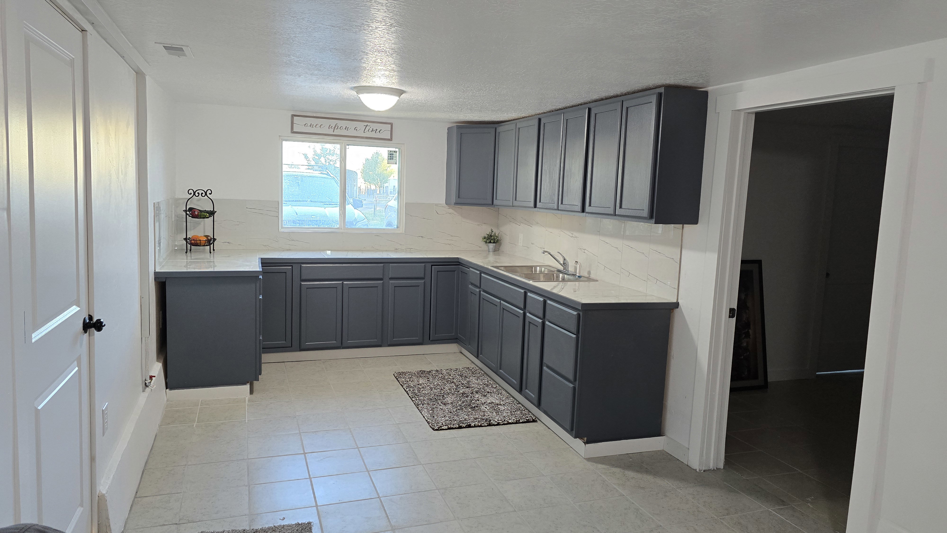 Kitchen featuring ample dark gray cabinetry, light-toned countertops, a white tile backsplash, and a stainless steel sink with a single-handle faucet