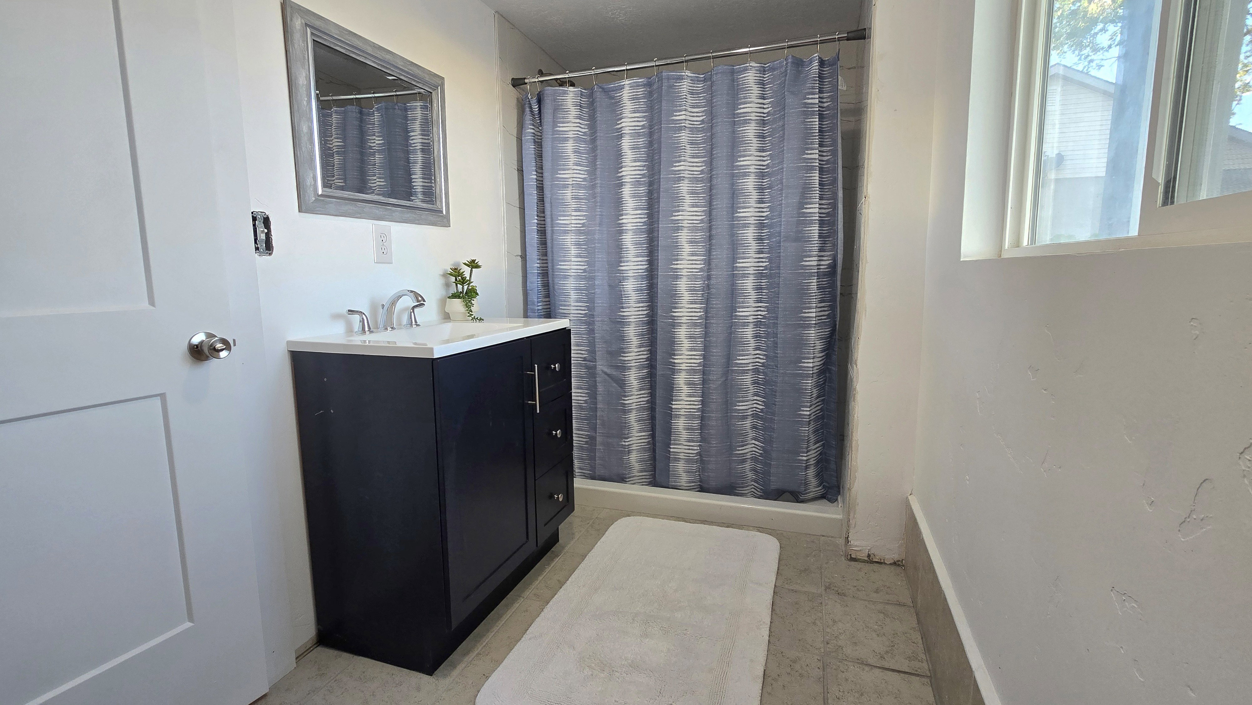 Bathroom featuring a dark vanity with a white countertop, a mirrored medicine cabinet, a shower with a shower curtain, and a window providing natural light