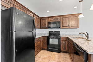 Kitchen with black appliances, light stone countertops, a peninsula, decorative light fixtures, and recessed lighting
