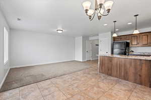 Kitchen with freestanding refrigerator, hanging light fixtures, light stone counters, open floor plan, and light colored carpet