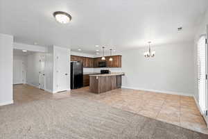 Kitchen featuring light tile patterned flooring, open floor plan, pendant lighting, black appliances, and light carpet