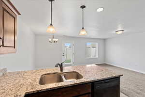 Kitchen featuring dishwasher, light stone countertops, light colored carpet, decorative light fixtures, and a textured ceiling