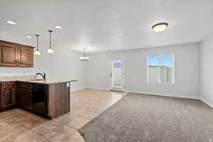 Kitchen featuring dark brown cabinetry, hanging light fixtures, a chandelier, dishwasher, and light stone countertops