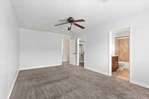 Unfurnished bedroom featuring a spacious closet, light colored carpet, a ceiling fan, and ensuite bath