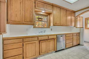 Kitchen featuring tile countertops, healthy amount of natural light, backsplash, dishwasher, and crown molding