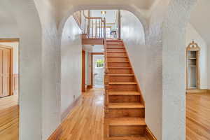 Stairs with a textured wall, wood finished floors, arched walkways, and a towering ceiling