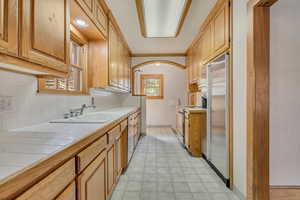 Kitchen with tile countertops, stainless steel fridge, decorative backsplash, stove, and crown molding