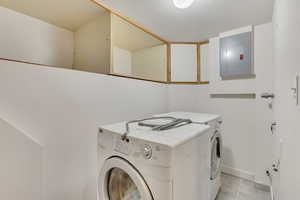 Laundry area featuring electric panel, light tile patterned floors, and washing machine and clothes dryer