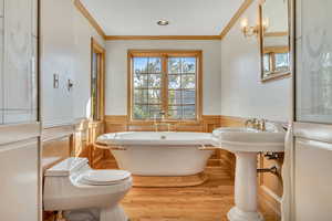 Bathroom with a freestanding tub, ornamental molding, light wood-type flooring, plenty of natural light, and wainscoting