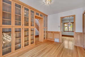 Spare room with wainscoting, a chandelier, light wood-style flooring, and stairs