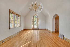 Empty room with a textured wall, a chandelier, wood finished floors, vaulted ceiling, and arched walkways