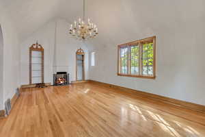 Unfurnished living room with light wood-type flooring, a chandelier, a multi sided fireplace, high vaulted ceiling, and built in shelves