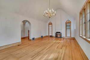 Unfurnished living room with light wood-style flooring, arched walkways, a chandelier, a multi sided fireplace, and high vaulted ceiling