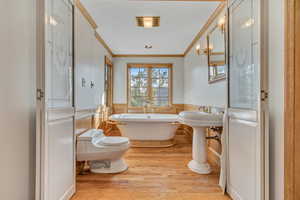 Full bath with a soaking tub, ornamental molding, light wood finished floors, and wainscoting