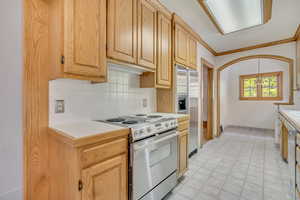Kitchen with tile counters, appliances with stainless steel finishes, backsplash, ornamental molding, and light tile patterned floors