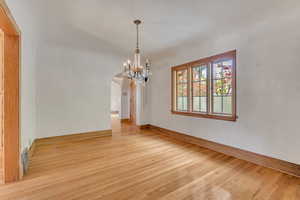 Unfurnished dining area with arched walkways, light wood finished floors, and a chandelier