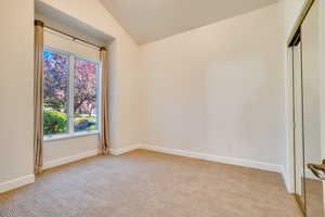 Empty room featuring light colored carpet and lofted ceiling